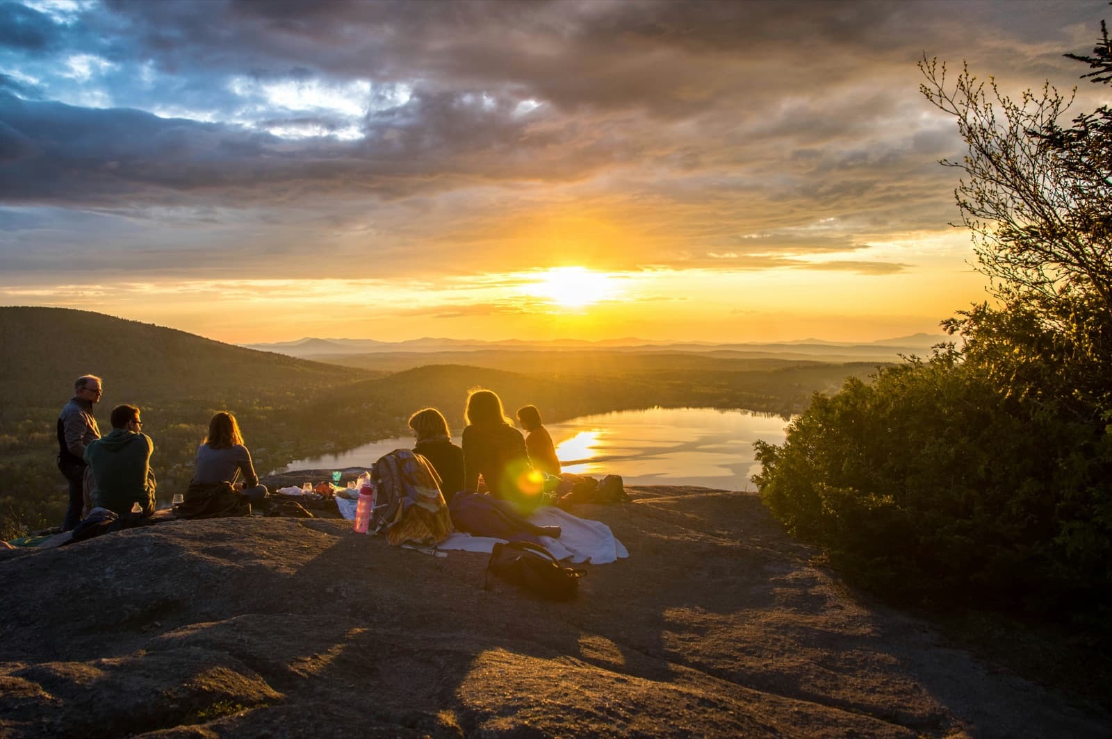 A small group gathered outdoors at sunset overlooking a lake
